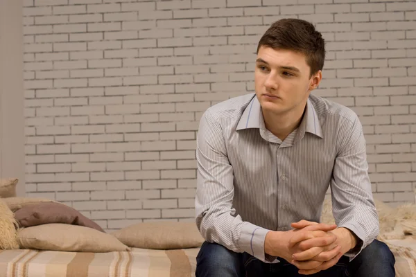 Junger Mann sitzt auf einem Sofa und denkt — Stockfoto