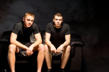 Two attractive young men on a black sofa clipart