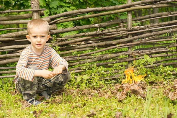 Handsome young boy squatting alongside a fire — Stock Photo, Image