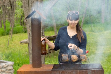 Attractive woman cooking over a picnic BBQ clipart