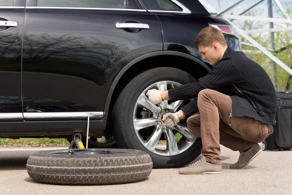 Young man changing the punctured tyre on his car — Stock Photo, Image