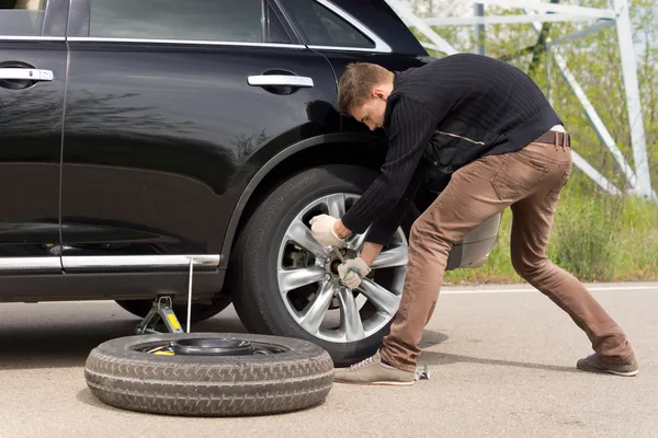 Jeune homme luttant pour changer son pneu de voiture — Photo