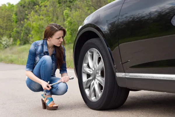 Mujer joven mirando un neumático pinchado en su coche — Foto de Stock