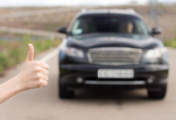 Woman giving a thumbs up as she stands hitchhiking
