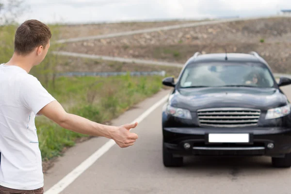 Young man hitching a lift on a country road — Stock Photo, Image