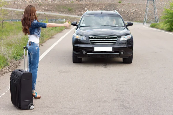 Młoda kobieta autostopem z walizką — Zdjęcie stockowe