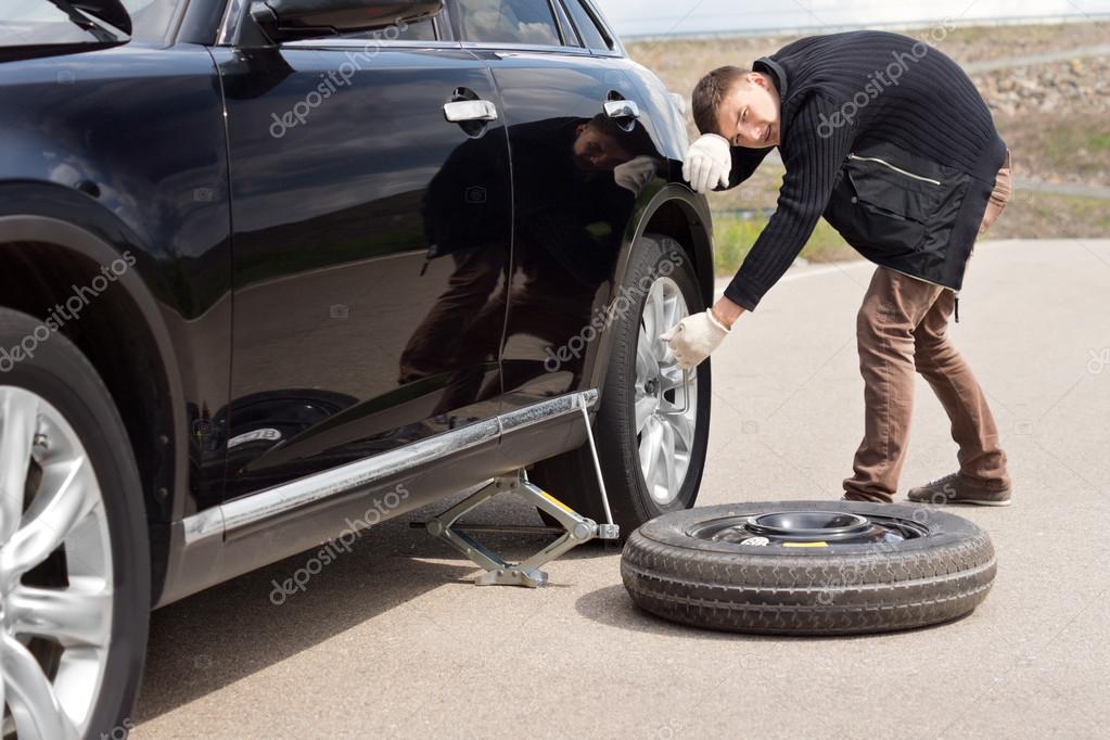 Male driver struggling to change his car tyre Stock Photo by