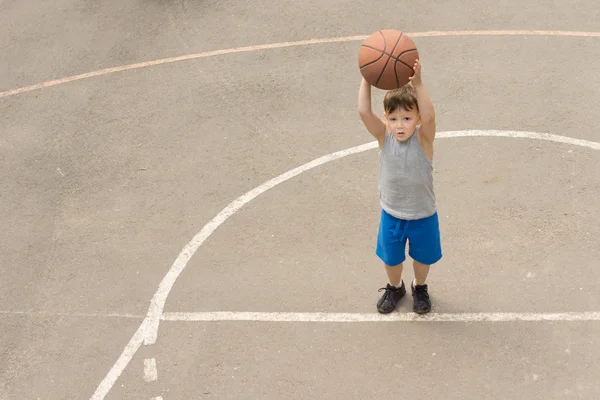 Söt liten pojke utövar på en basketplan — Stockfoto