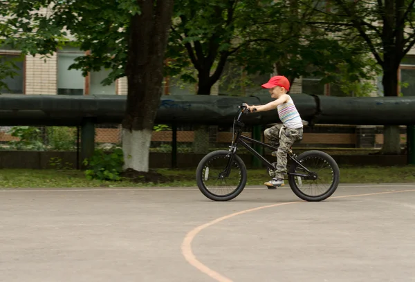 年轻的男孩在篮球场上骑他的自行车 — 图库照片