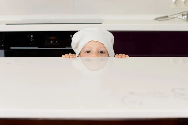 Мальчик в шляпе шеф-повара, заглядывающий за прилавок — стоковое фото