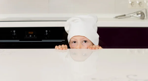 Ребенок в костюме шеф-повара прячется за прилавком — стоковое фото