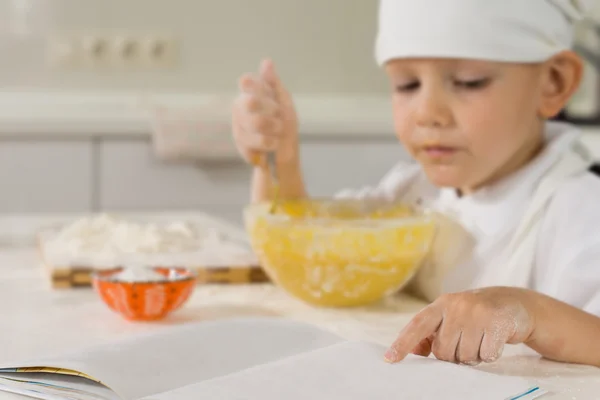 Petit garçon lisant un livre de recettes pendant qu'il cuit — Photo