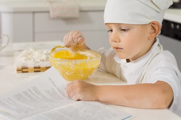 Carino piccolo ragazzo che legge una ricetta mentre cucina — Foto Stock