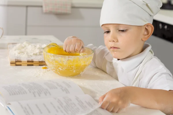 Chef menino verificando sua receita como ele assa — Fotografia de Stock