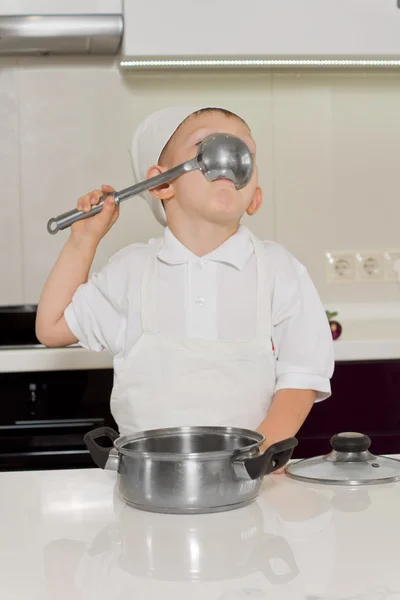 Cute little boy chef tasting the recipe — Stock Photo, Image