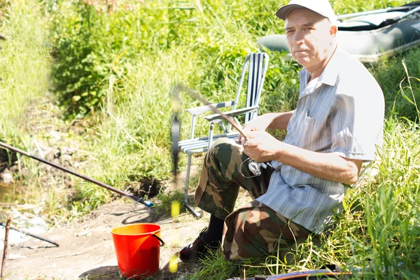 Elderly disabled man sitting fishing at a lake — Stock Photo, Image