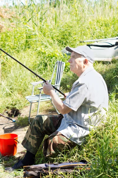 Elderly disabled man fishing on a river bank — Stock Photo, Image