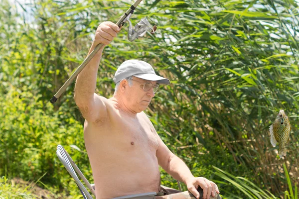 Senior fisherman dangling a fish on his line — Stock Photo, Image