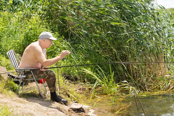 Idoso pesca cuidadosamente testando sua linha — Fotografia de Stock