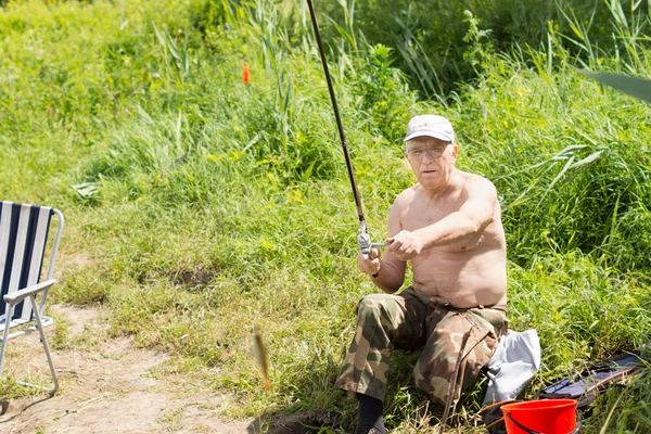 Elderly fisherman reeling in a small fish — Stock Photo, Image