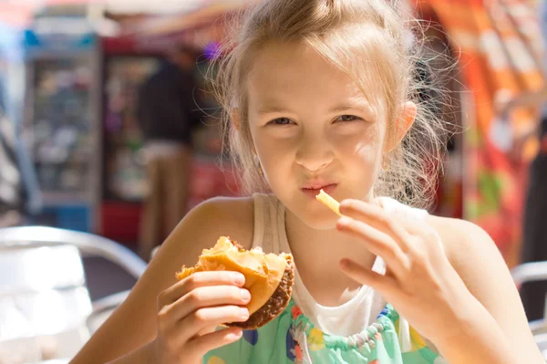 Girl eating French fries and a hamburger sandwich — Stock Photo, Image