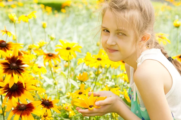 Lächelndes hübsches kleines Mädchen inmitten von Sommerblumen — Stockfoto