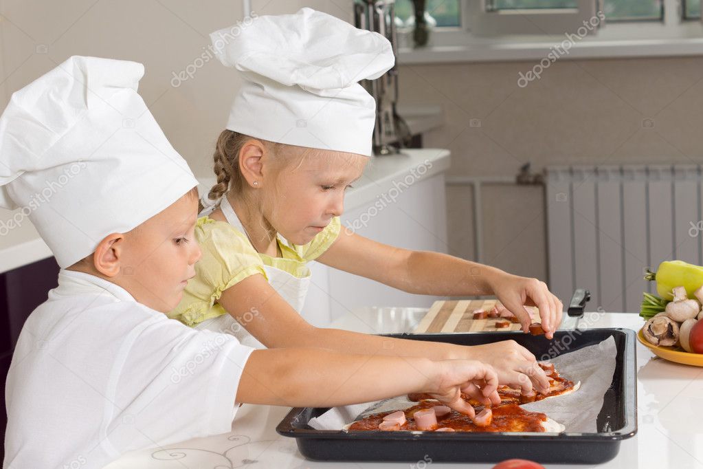 Young girl and boy loading ingredients onto pizza