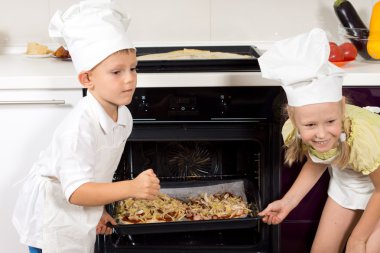 Happy children putting their pizzas in the oven clipart
