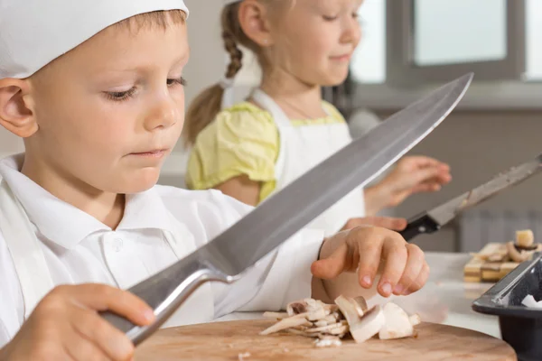 Kleiner Junge schwingt ein großes Messer und hackt Pilze — Stockfoto