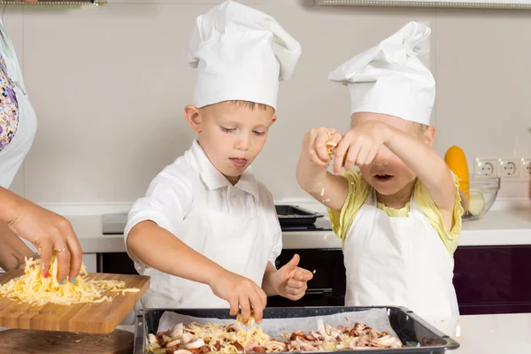 Niedliche kleine Kinder setzen Käse auf Pizza — Stockfoto