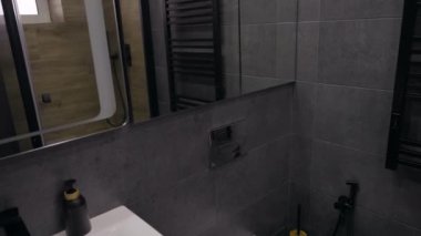 Kırpılmış bir manzarada tek el leğeni, aynası, gösterişi ve tuvaleti olan bir apartman dairesinde ya da evde bulunan küçük gri fayanslı bir banyonun içi.