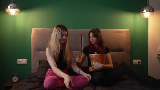 Dos mujeres jóvenes relajándose en una cama con una bañera de palomitas de maíz — Vídeos de Stock
