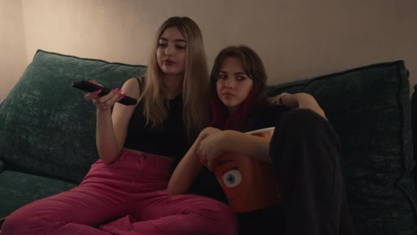 Дві молоді сестри або друзі розслабляються на дивані, дивлячись телевізор — стокове відео