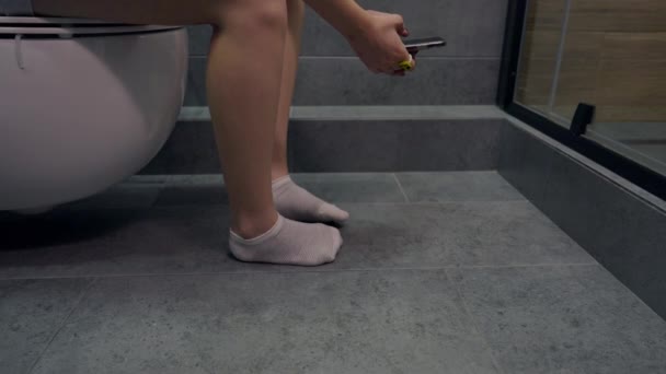 Молодая женщина, сидящая на унитазе или в туалете — стоковое видео