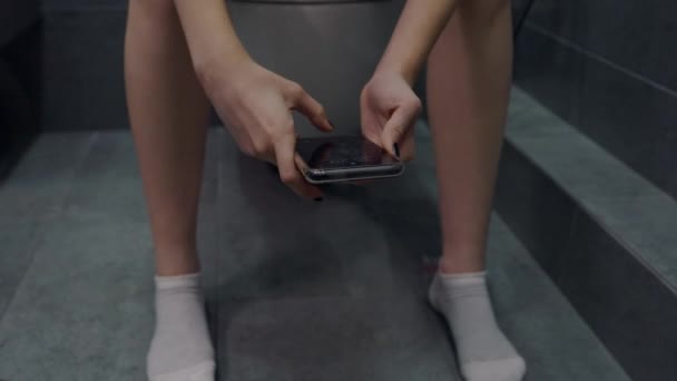 Mujer joven sentada en un inodoro usando su teléfono móvil — Vídeos de Stock