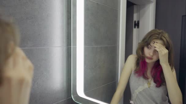 Schläfrige junge Frau, die sich selbst im Spiegel betrachtet — Stockvideo