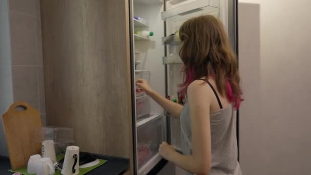 Junge Frau bereitet in der Küche eine Mahlzeit zu und schaut in einen Kühlschrank — Stockvideo