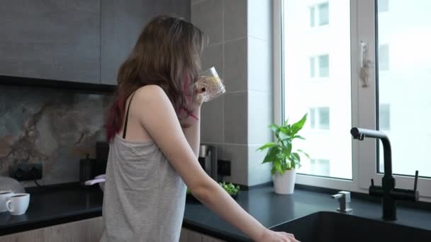 Молода жінка стоїть з вікна своєї квартири — стокове відео