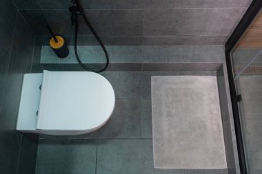 Kapalı bir tuvalet, banyo paspası ve duş kabini olan küçük gri fayanslı bir apartman dairesi.