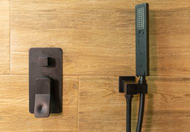 Duş başlığı ve mikser musluğu bir duş bölmesinde duvarda ahşap desenli fayanslar var.