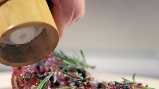 Person grinding peppercorns onto raw meat for seasoning — Stock Video