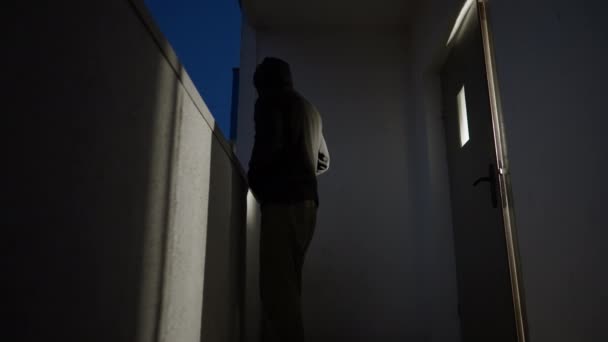 Furtive man in hoodie standing outside apartment door at night — Stock Video