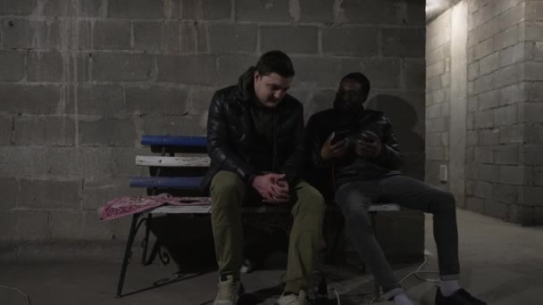 白人男性と黒人男性は 爆弾避難所に座っており 戦争のニュースを議論しています ウクライナでのロシアの侵略 — ストック動画