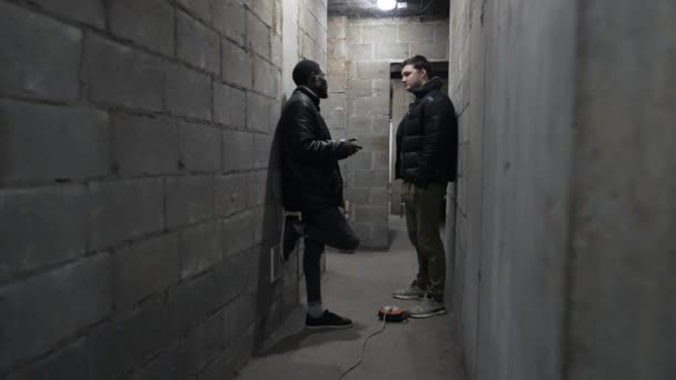 Vit kille och svart kille står i ett skyddsrum och pratar under rysk invasion. — Stockvideo