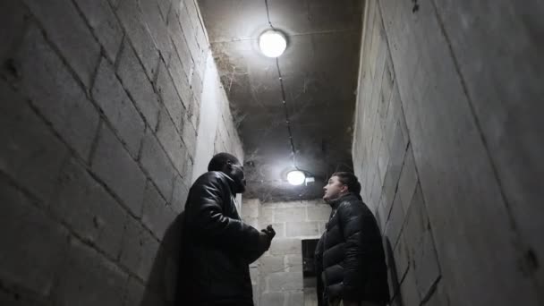 Blick auf einen Luftschutzbunker mit der Decke im Spinnennetz, Kaukasier und Schwarzer unterhalten sich während eines Bombardements über den Krieg — Stockvideo