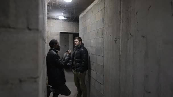 Vista de un refugio antibombas con un tipo caucásico y un tipo negro conversando sobre la guerra durante un bombardeo — Vídeos de Stock