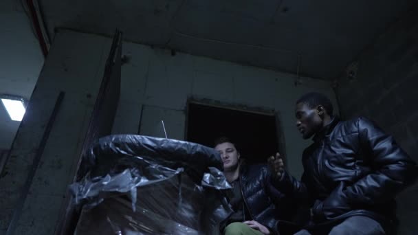 Кавказький хлопець і чорний хлопець переховуються в підвалі під час війни і обговорюють останні новини — стокове відео