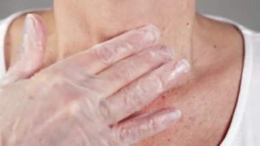 Yaşlı bir kadın, steril eldivenle eldivenli bir elle boğazına dokunuyor.