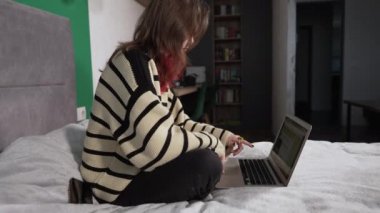 Young redhead woman sitting in a bed working on a laptop
