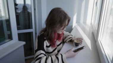 Genç kız bir mesaj okurken kahve içiyor.